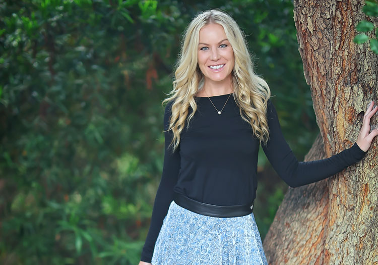 Smiling blonde woman leaning on tree outdoors